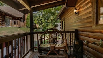 A wooden porch with a rocking chair, a small bear statue, and a window with a view of a house and trees.