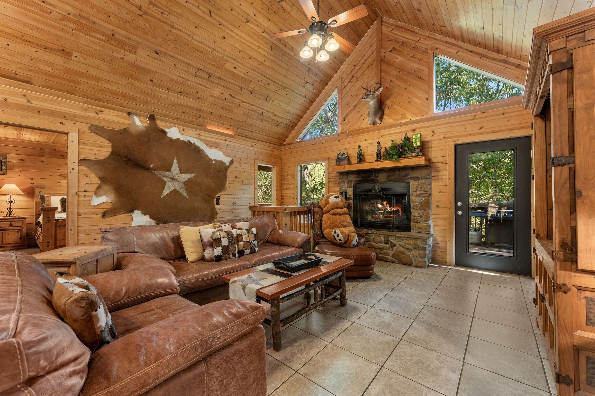 A cozy cabin interior with a leather sofa, a stone fireplace, and a bear statue.