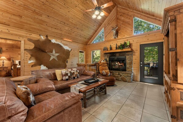 A cozy cabin interior with a leather sofa, a stone fireplace, and a bear statue.
