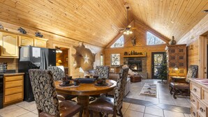 A log cabin interior with a dining area, kitchen, and fireplace. - Upscale Log Cabin Over 2400 Sq Ft- Game Table-Free Tickets-Hot Tub-Car Charger-Near Thunder Ridge (Ridgedale)