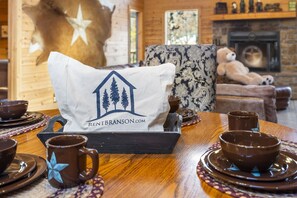 A dining table set with brown mugs and bowls, a white pillow with a logo, and a bear statue in the background. - Upscale Log Cabin Over 2400 Sq Ft- Game Table-Free Tickets-Hot Tub-Car Charger-Near Thunder Ridge (Ridgedale)