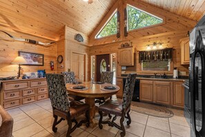 A wooden cabin interior with a dining area, kitchen, and a large window.