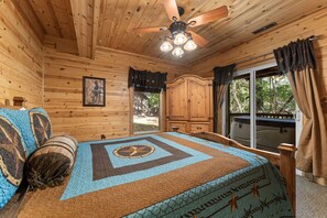 Un dormitorio de cabaña de madera con cama, ventilador de techo y ventana con cortinas.
