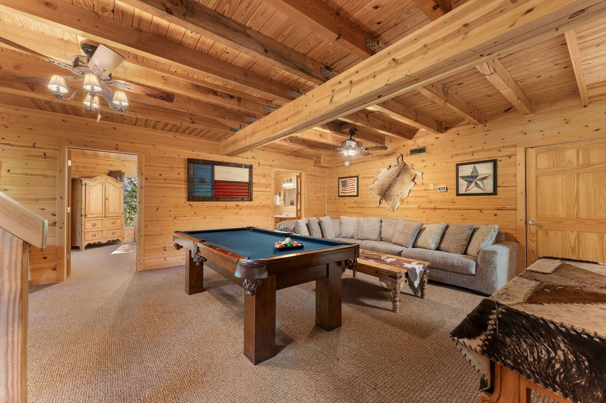 A wooden interior with a pool table, sofa, and ceiling fans.