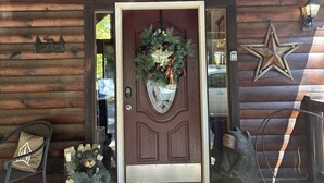 A wooden cabin entrance with a decorative wreath, a star decoration, and a bear sculpture on the porch. - Upscale Log Cabin Over 2400 Sq Ft- Game Table-Free Tickets-Hot Tub-Car Charger-Near Thunder Ridge (Ridgedale)