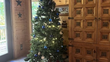 A wooden cabin interior with a decorated Christmas tree, a wooden cabinet, and a rug with a lion design.