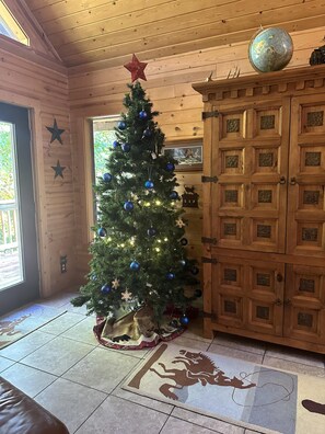 A wooden cabin interior with a decorated Christmas tree, a wooden cabinet, and a rug with a lion design. - Upscale Log Cabin Over 2400 Sq Ft- Game Table-Free Tickets-Hot Tub-Car Charger-Near Thunder Ridge (Ridgedale)