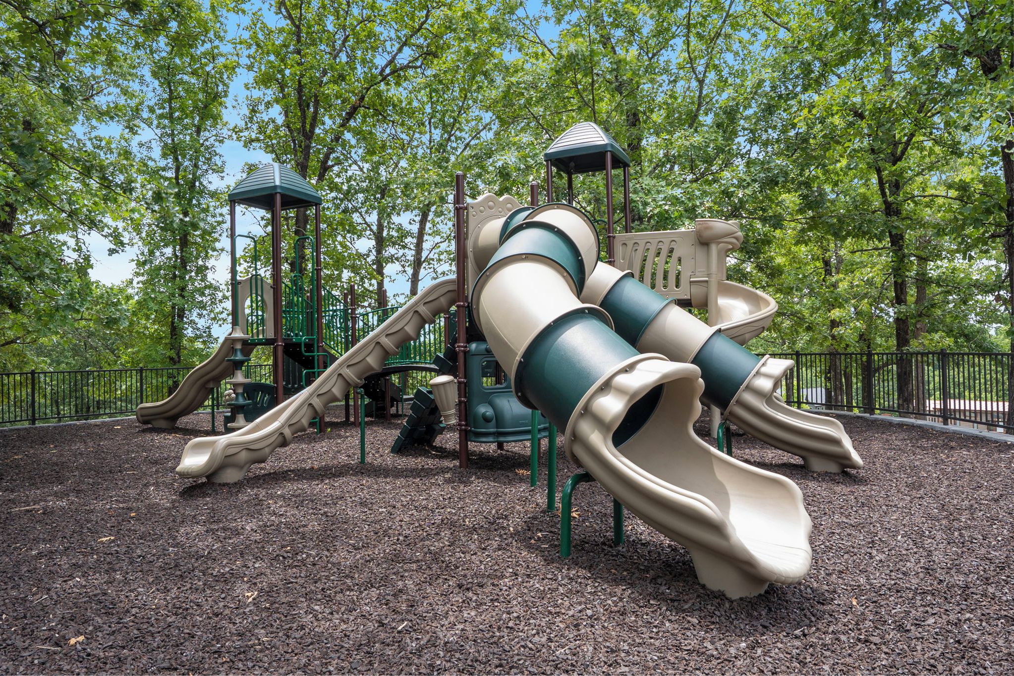 A playground with slides and climbing structures surrounded by trees.
