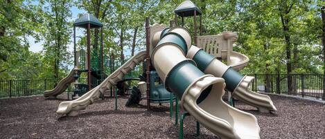 A playground with slides and climbing structures surrounded by trees.