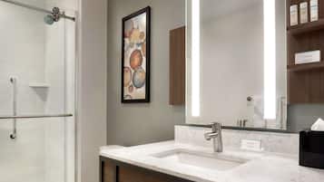 A modern bathroom with a shower, a large mirror, a marble sink, and a framed artwork on the wall.