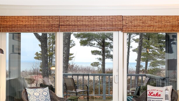 A room with a large sliding glass door leading to a deck with outdoor seating and a view of the beach and ocean.