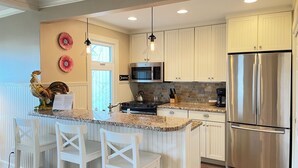 A modern kitchen with white cabinetry, a stainless steel refrigerator, a granite countertop, and a central island with bar stools.