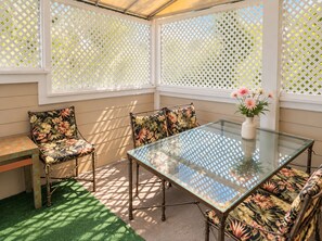 A conservatory with a glass table, floral chairs, and a white lattice screen.
