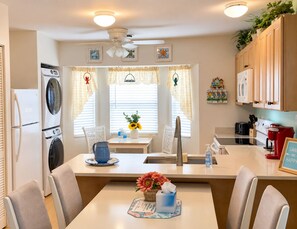 Une cuisine compacte dotée d’un îlot central, d’un lave-linge et d’un sèche-linge intégrés, ainsi que d’un coin repas avec une table et des chaises.