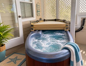 A spa area with a hot tub, a wooden bench, a star-patterned mat, and a potted plant. - Key West Oasis on Duval Street : Private Hot Tub • Pool • Parking • 2 Balconies (Key West)