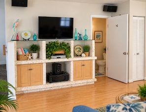 A living room with a flat-screen TV, a coffee table, a sofa, and a door leading to a bathroom.