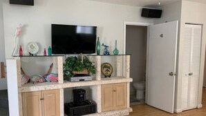 Ein Wohnzimmer mit Fernseher auf einer Glasablage, einer Kaffeemaschine und einer Tür zu einem Badezimmer.
