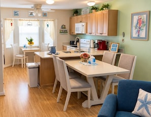 A modern kitchen with white cabinets, a microwave, and a coffee maker. There is a dining area with a table and chairs, and a blue sofa in the living room.
