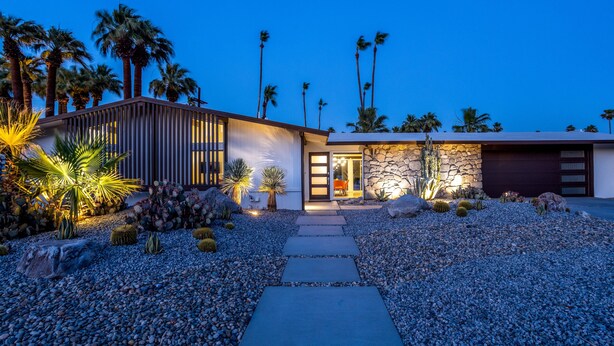A modern house with a stone facade, a wooden deck, and a gravel driveway. - Alexander Sunrise - Luxury Midcentury Retreat (Palm Springs)