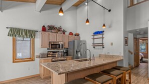 Une cuisine moderne dotée d’un grand îlot central, d’appareils électroménagers en acier inoxydable et de tabourets de bar en bois.