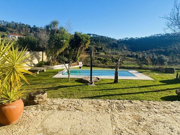 Uma área de piscina com um deck de pedra, cercada por um gramado e árvores.