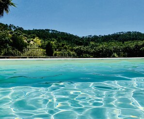 Piscina translúcida com ondulações visíveis e uma colina arborizada ao fundo.