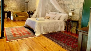Une chambre à coucher avec un lit à baldaquin, un mur en pierre, un plafond en bois et un tapis à motifs rouges et blancs.