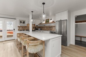 A modern kitchen with a large island, stainless steel appliances, and wooden bar stools with fur seats. - Ski In/Out, Fully Remolded Ground Floor, Ski Shuttle + EZCancel (Steamboat Springs)