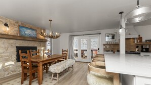 Eine moderne Küche mit Kamin aus Stein, einem Holzespeisetisch und einer großen Kochinsel mit weißer Arbeitsplatte.