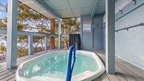 Ein Whirlpool auf einer Holzterrasse mit einem Sicherheitsschild und Blick auf Bäume.
