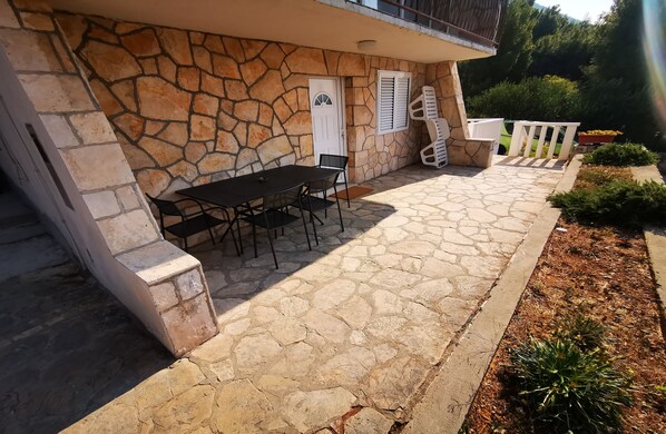 A stone building with a patio area featuring a table and chairs, a door, and a window with shutters.