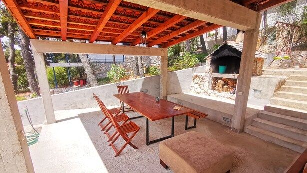 Eine Terrasse im Freien mit einem Holztisch und -stühlen, einer gepolsterten Bank und einem Steinkamin.