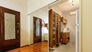 A hallway with a wooden herringbone floor, a mirrored closet door, and a kitchen area with a refrigerator, microwave, and wooden cabinets.