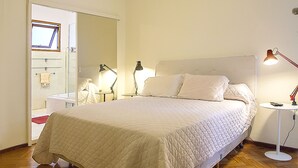 A bedroom with a bed, bedside lamps, a mirror, and a wooden floor.