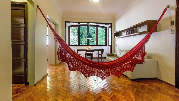 A room with a hammock, wooden flooring, a dining area, and a large window.