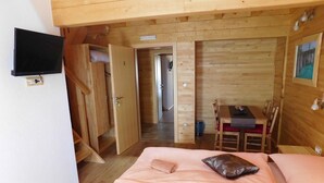 Una habitación de cabaña de madera con una cama, un televisor, una mesa de comedor y una silla.