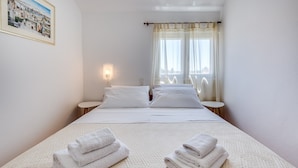 A hotel room with a bed, two bedside tables, a wall-mounted light, and a window with sheer curtains.