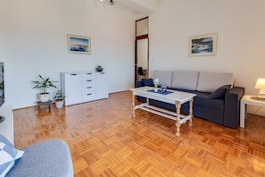 A living room with a sofa, a coffee table, a TV, and a kitchen area with cabinets and a plant. - Apartments Katica, (15095), Zadar, hr (Zadar)