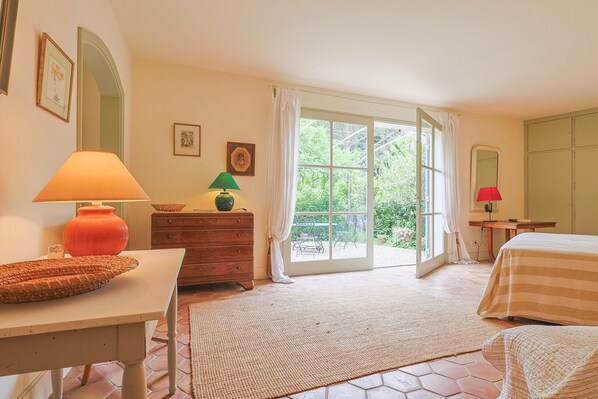 Une chambre à coucher comprenant un lit, un bureau, une commode et une fenêtre donnant sur un paysage verdoyant.