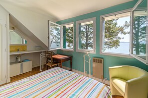 A bedroom with a bed, a desk, a chair, a window, and a view of the water.