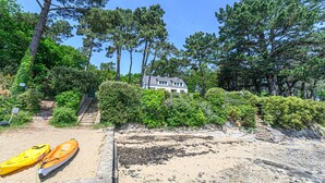 En strand med kajaker, ett hus omgivet av träd och en trappa som leder upp till huset.