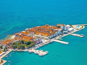 Vue aérienne d’une ville côtière avec un port de plaisance, des bâtiments aux toits rouges et une mer d’un bleu limpide.