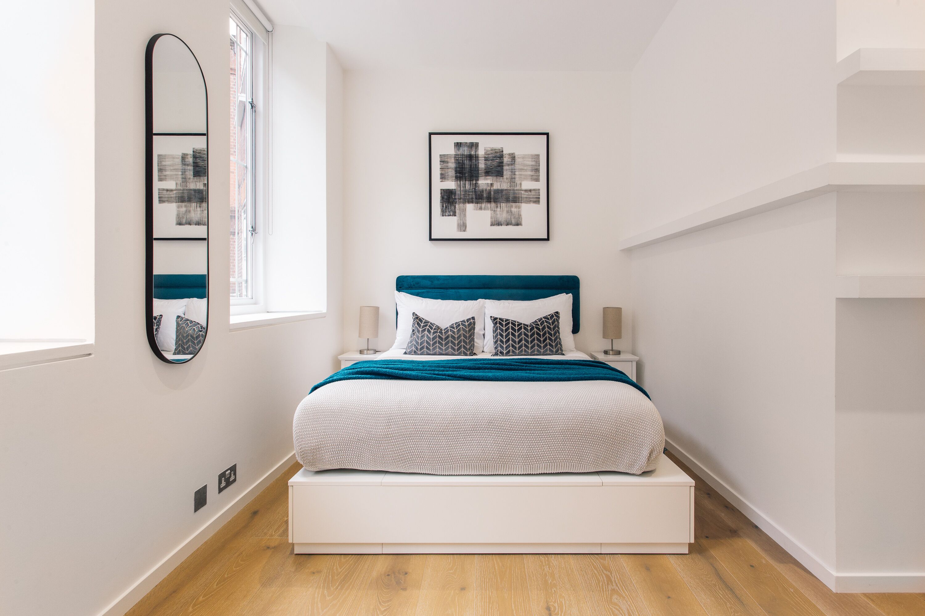 A modern bedroom with a bed, a mirror, and two framed artworks.