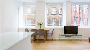 A modern living room with a glass coffee table, a flat-screen TV, and a dining area with chairs and a vase of flowers. - 2 Bed 2 Bath Apartment Off Regent Street (London)
