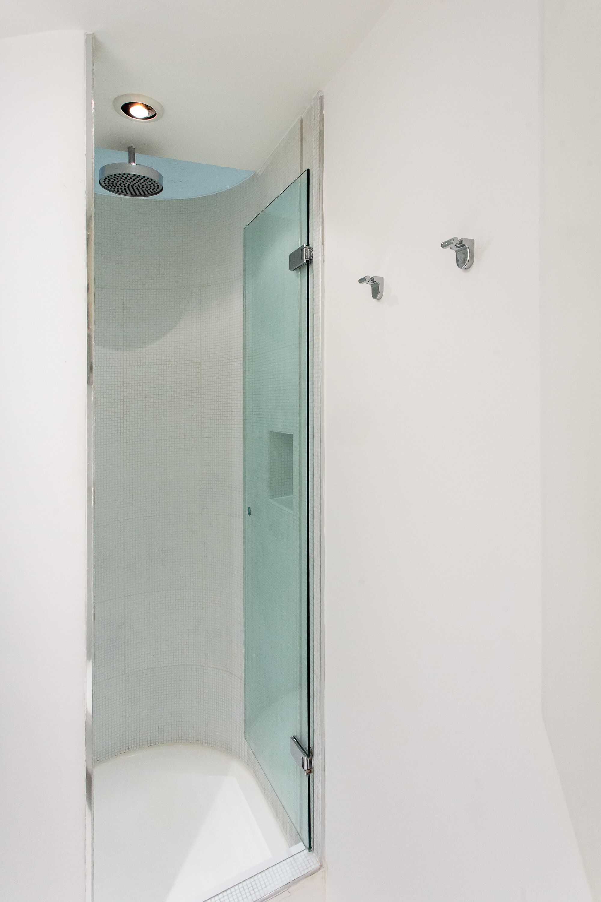 Een douche met glazen wanden, een daklamp, een betegelde hoek en een glazen deur.