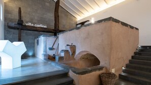 Interior rústico com parede de pedra, viga de madeira e escada.