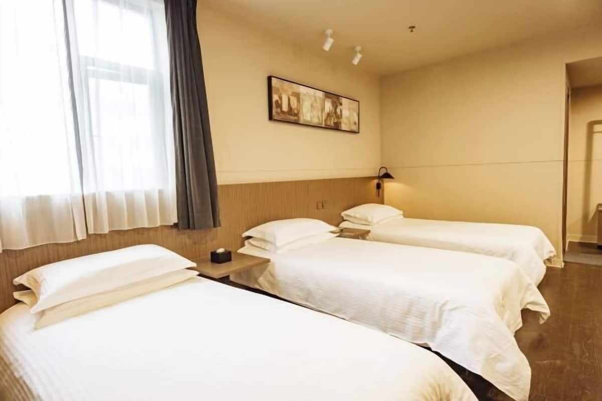 A hotel room with two beds, a nightstand, a lamp, a painting on the wall, and a window with curtains.