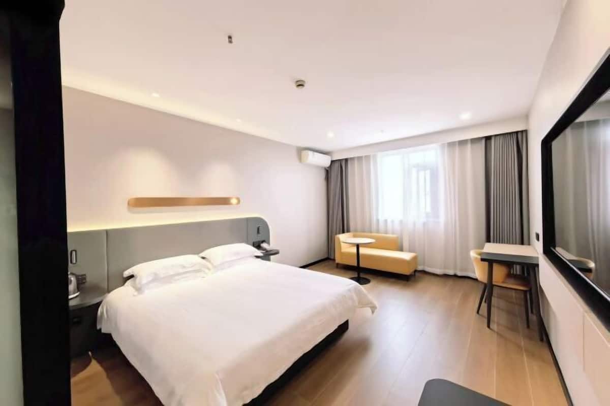 A modern hotel room with a large bed, a small round table, a sofa, and a TV.
