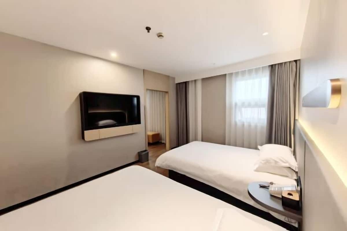 A hotel room with two beds, a TV, a bedside table, and a window with curtains.