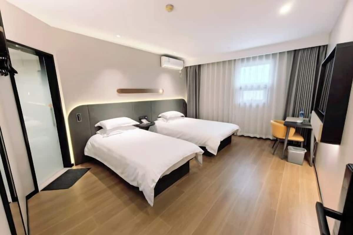 A hotel room with two beds, a desk, a chair, a TV, and a window with curtains.